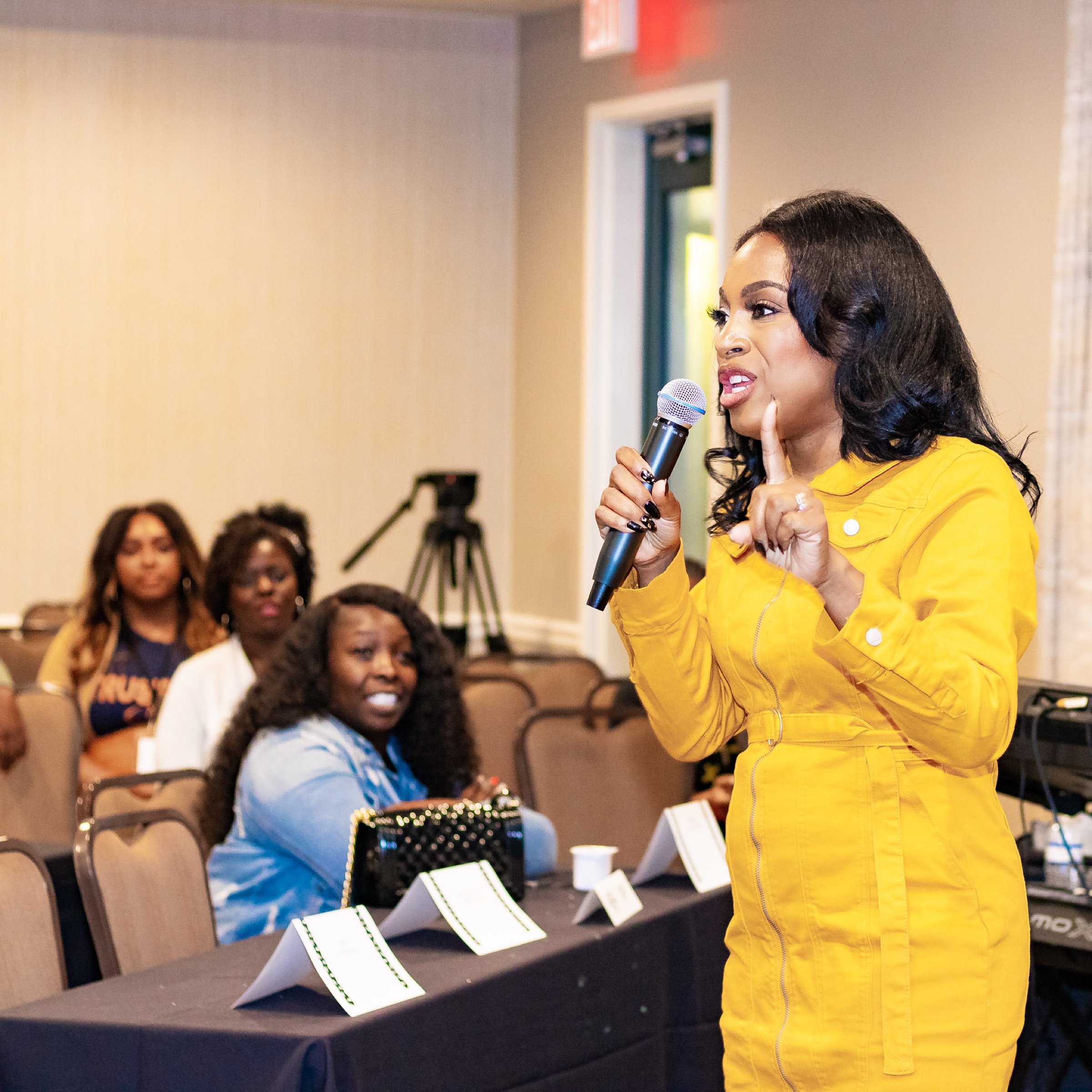 Chanel speaking to an audience in a yellow jumpsuit